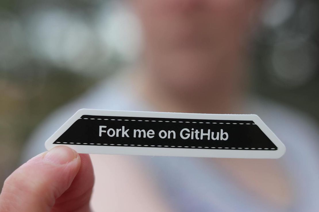 Fingertips hold a sign that reads: Fork me on Github